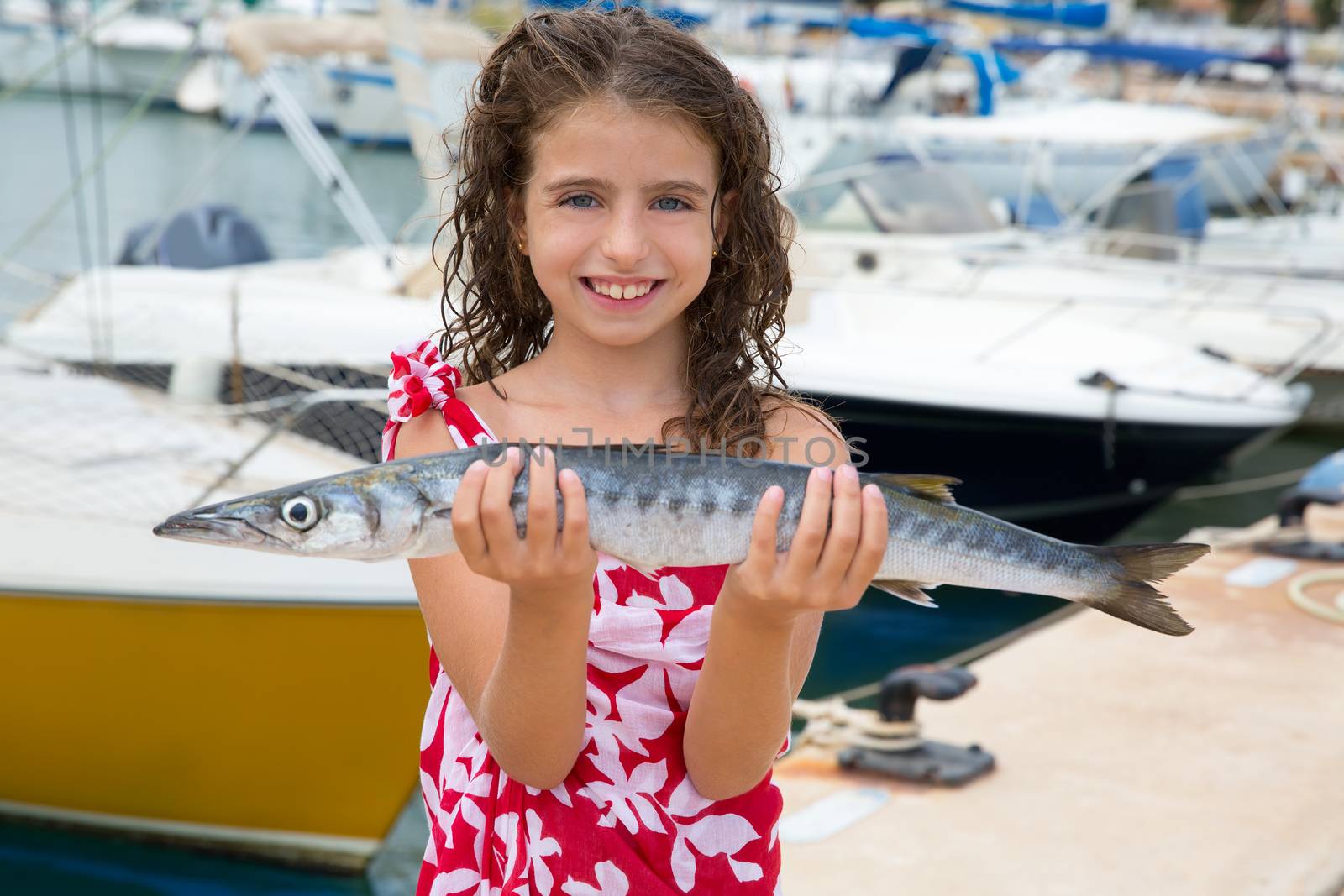 Happy kid fisherwoman with barracuda fish catch in Mediterranean marina