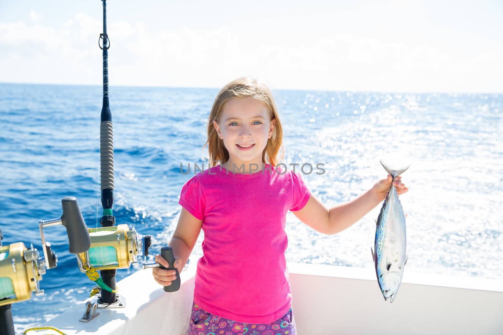 Blond kid girl fishing tuna little tunny happy with trolling catch on boat deck