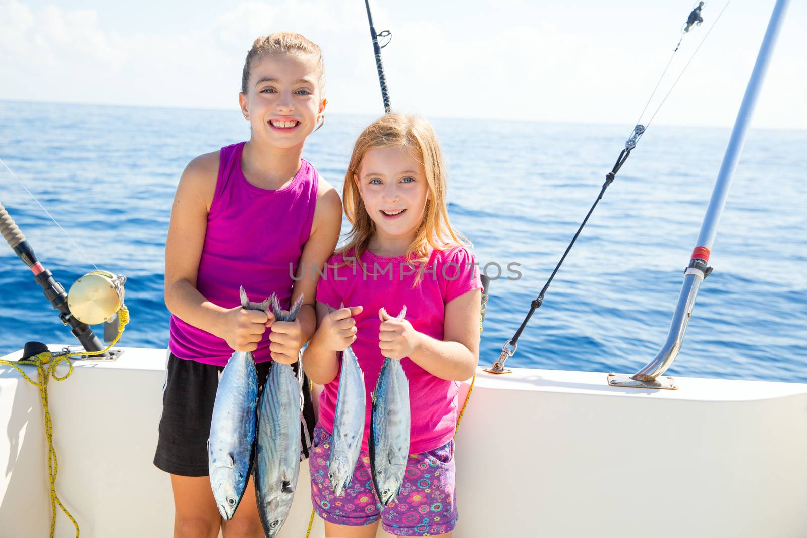 Happy tuna fisherwomen kid girls on boat with fishes trolling catch