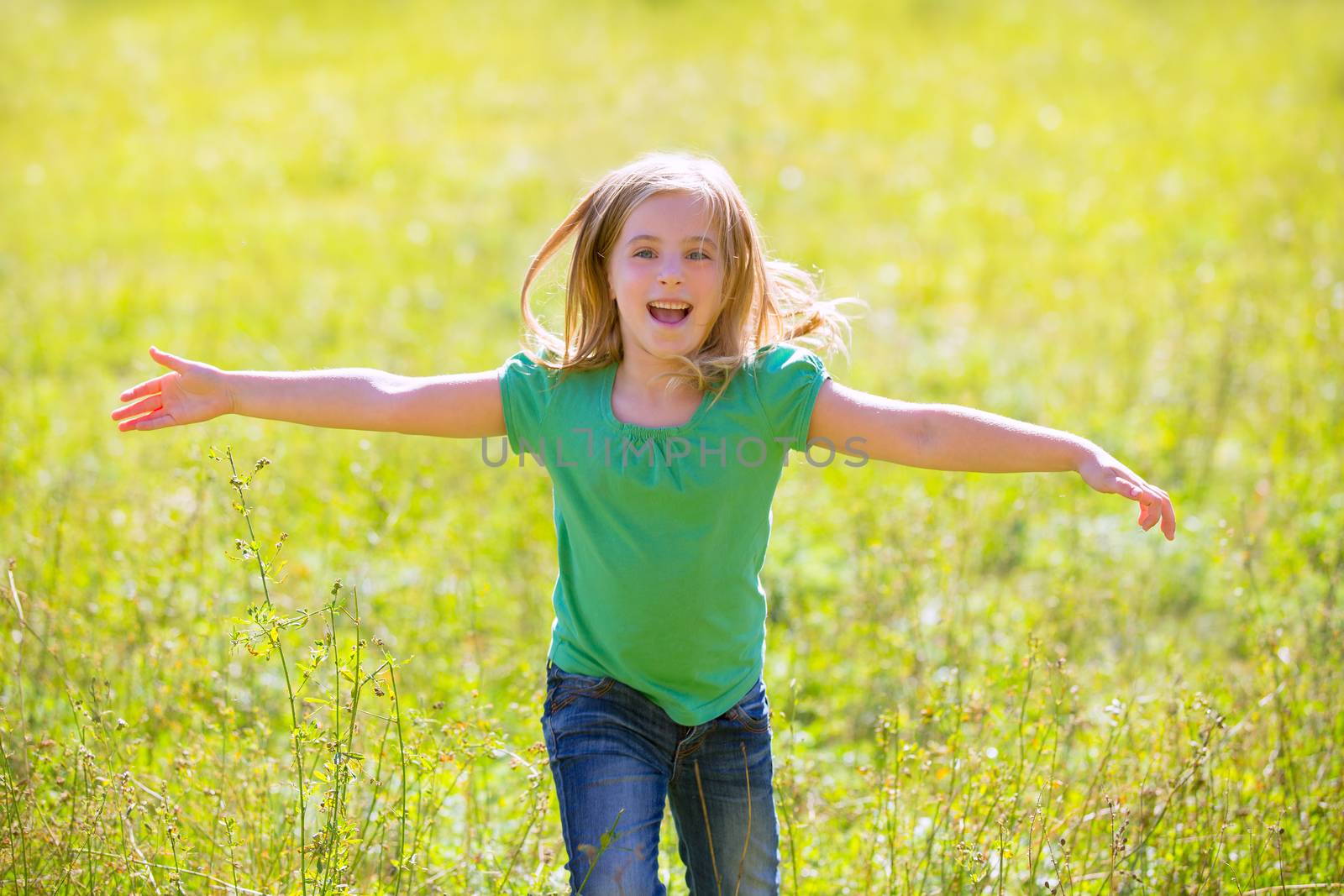 Blond kid girl happy running open hands smiling in outdoor green meadow