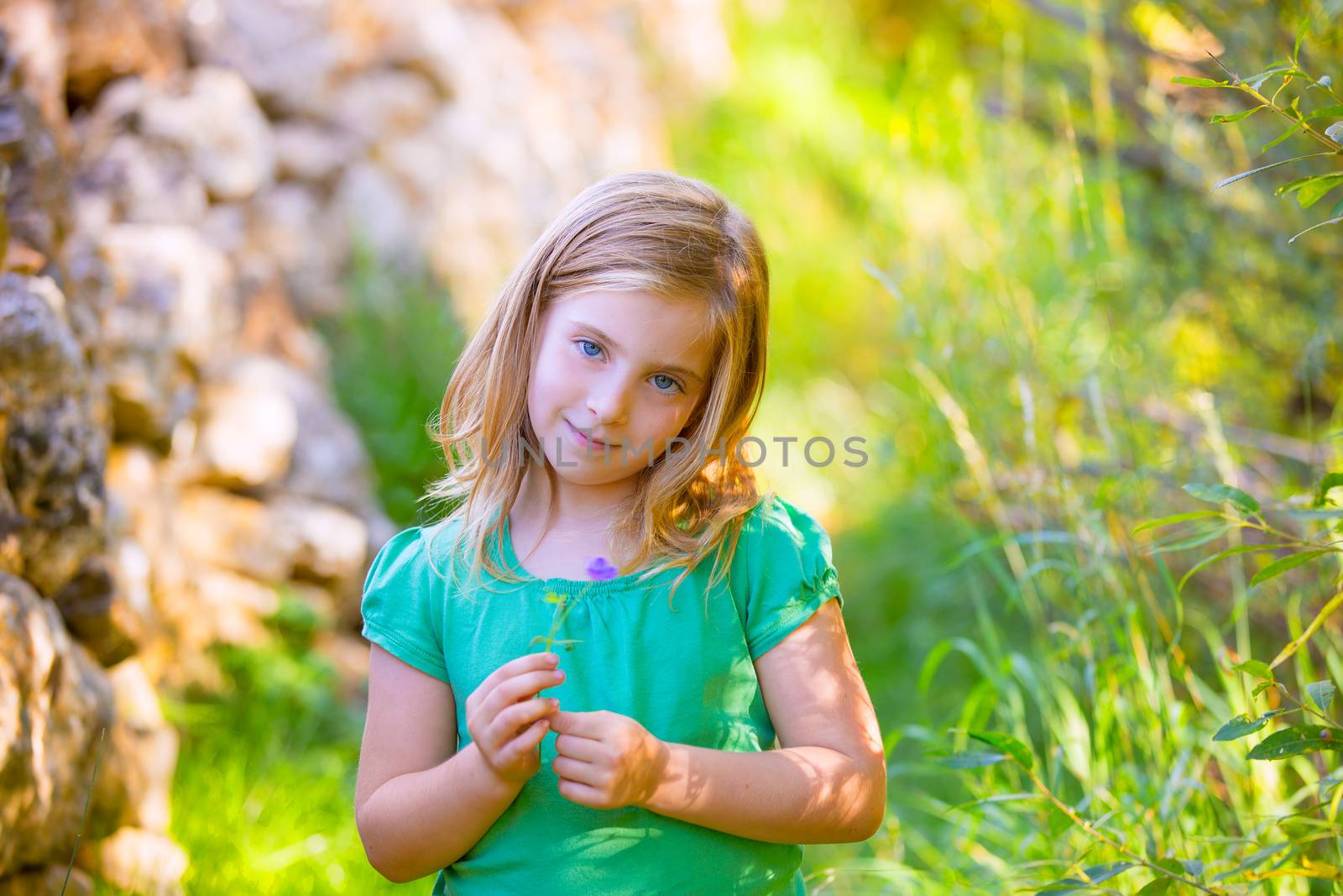 Blond kid girl smiling with purple flower relaxed outdoor by lunamarina