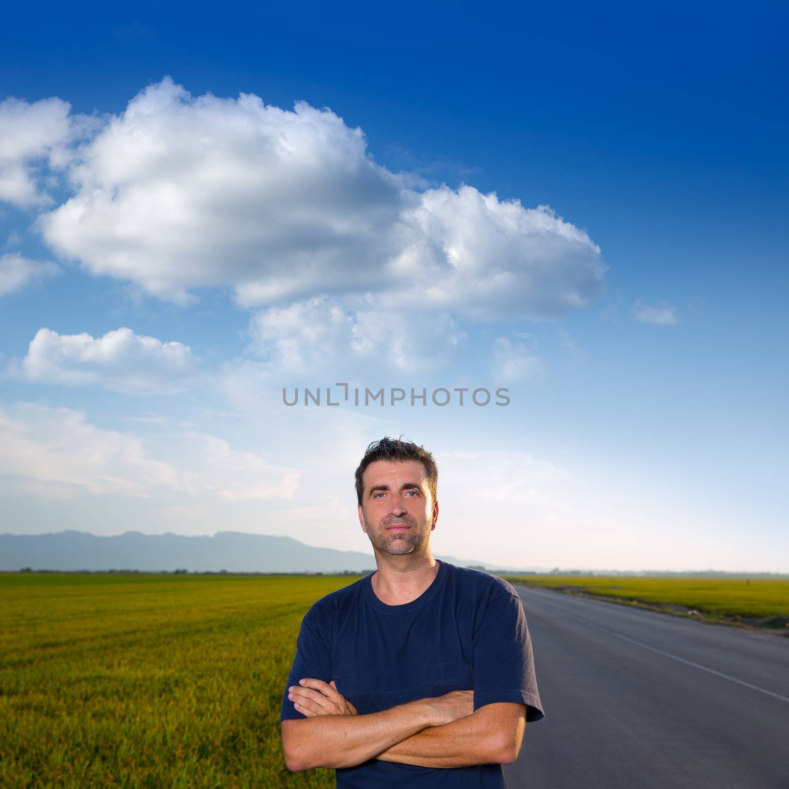 Mid age man in road at meadows posing with crossed arms cereal fields