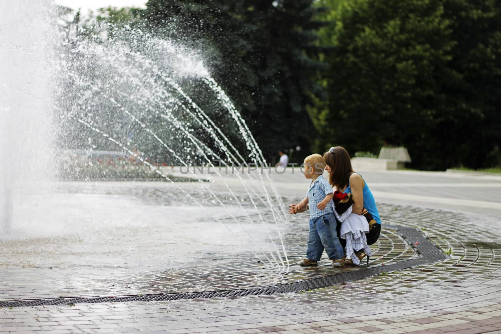Woman and child walking around splashing fontain in the center of the town