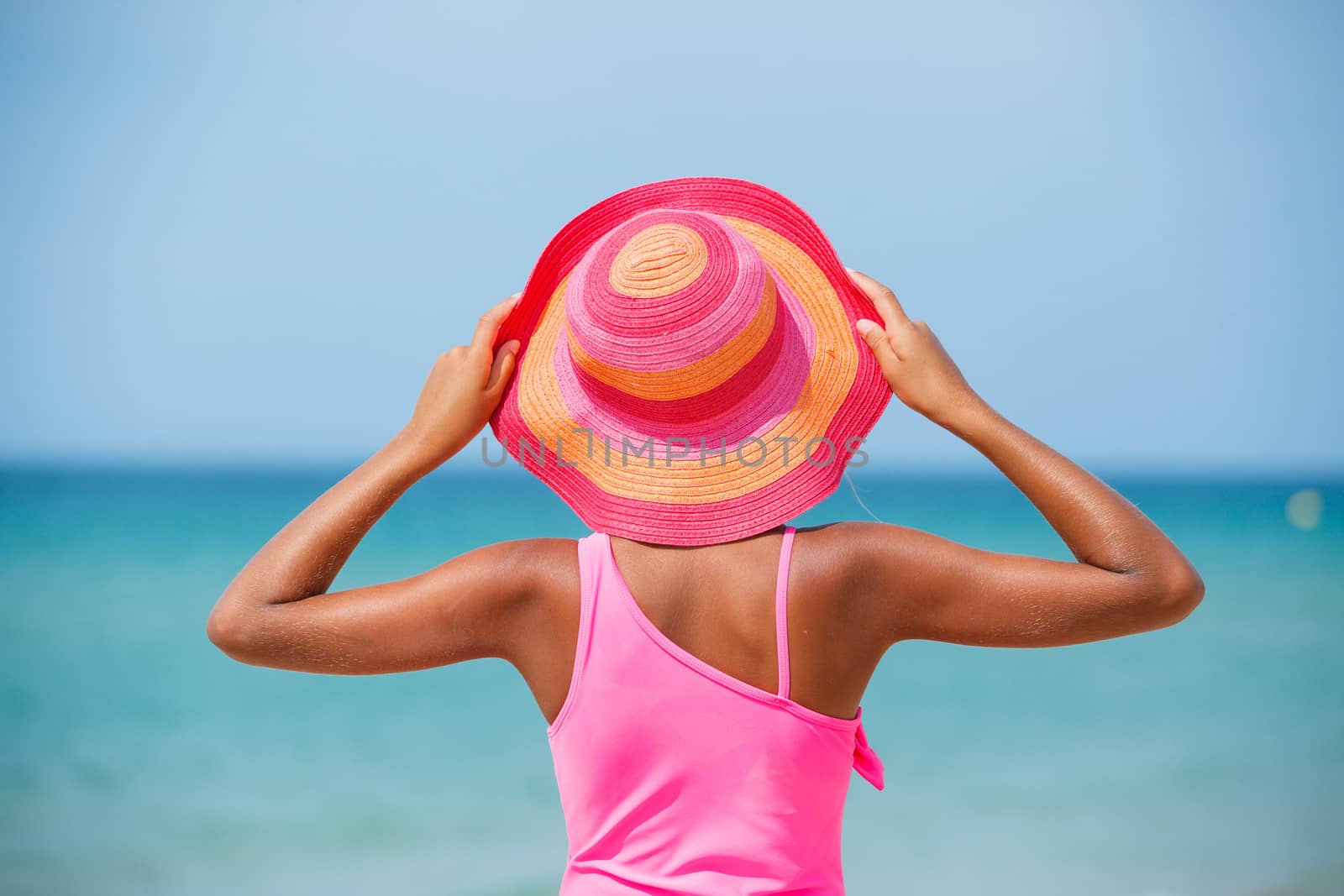 Back view of beautiful girl in pink hat and on background sea
