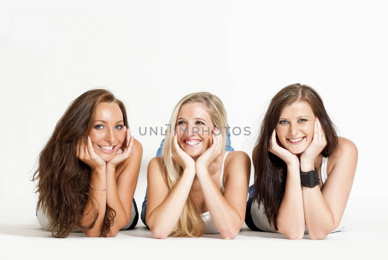 three young female friends lying on the floor, looking ar camera, smiling