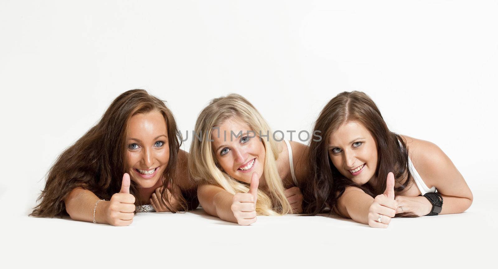 three young female friends lying on the floor showing thumbs up