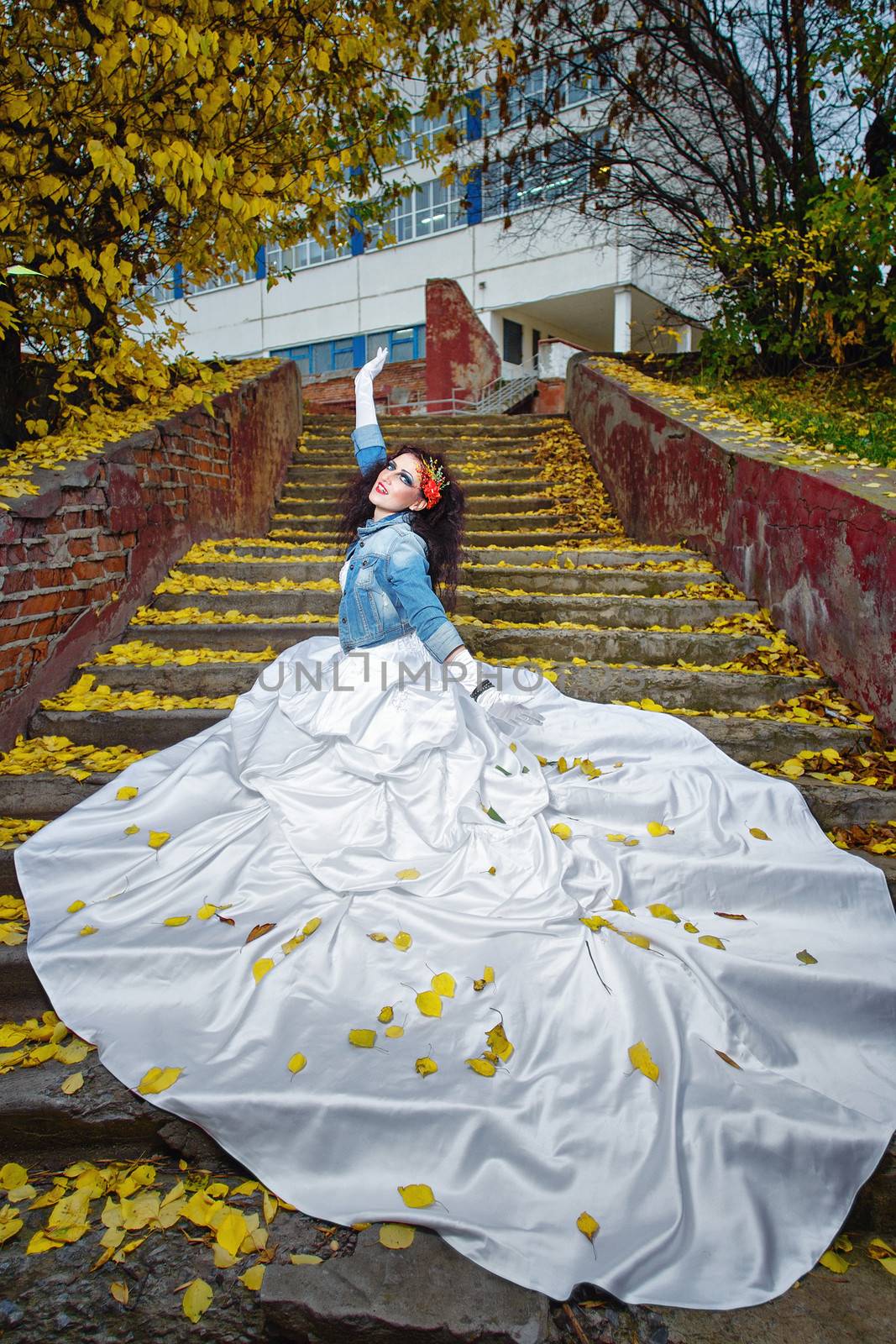 Beautiful bride in magnificent dress stands alone on stairs in autumn day