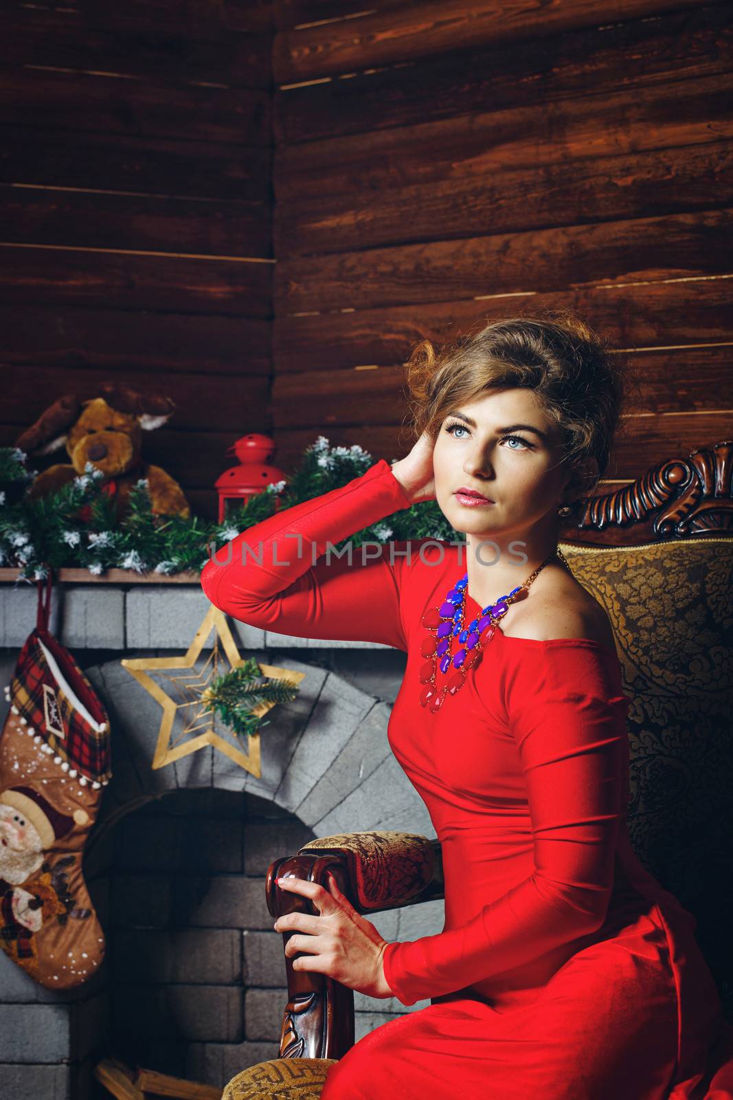 Attractive young girl in red dress sitting in armchair near fireplaces Christmas