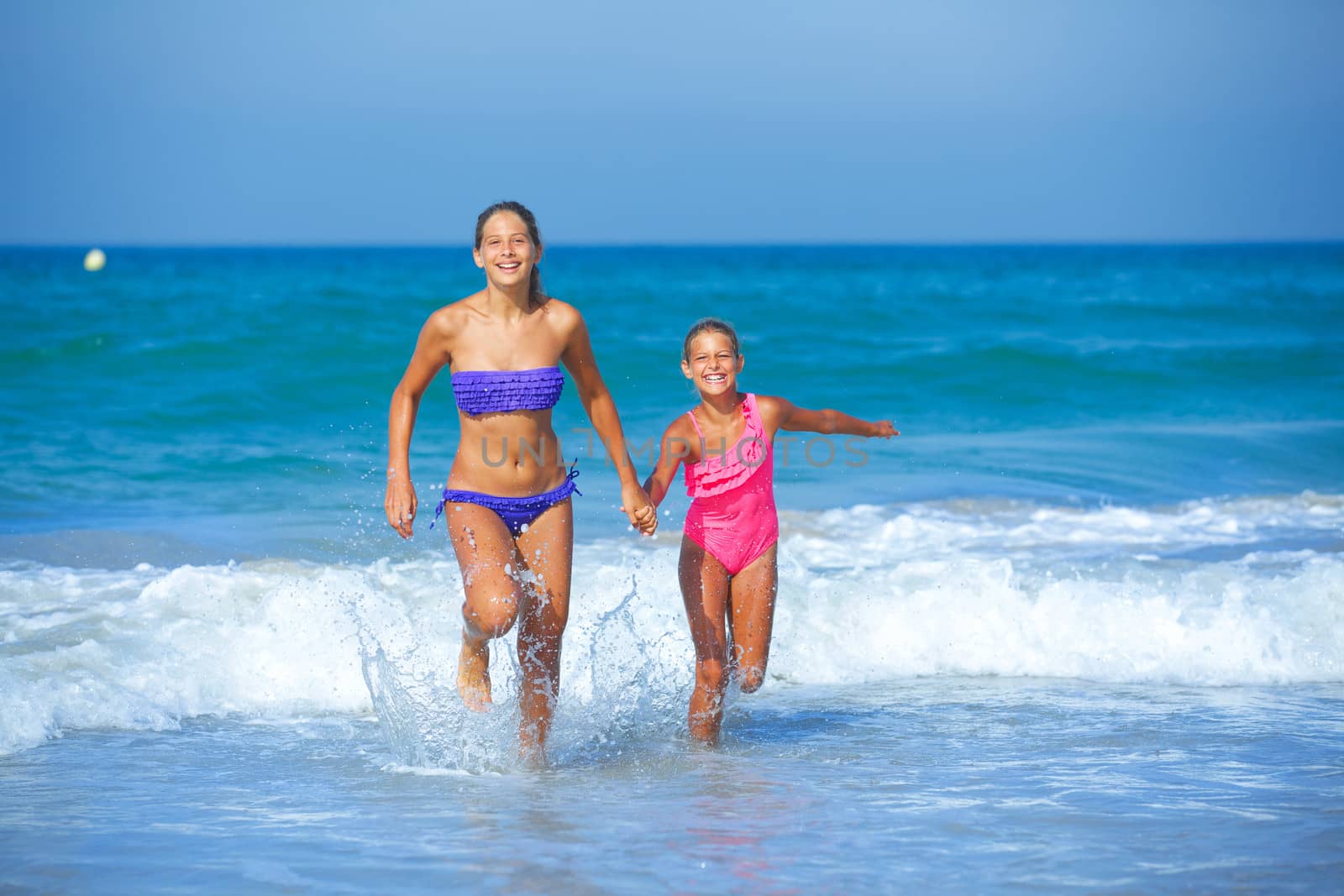 Cute girls friends running together in the beach shore on summer vacation