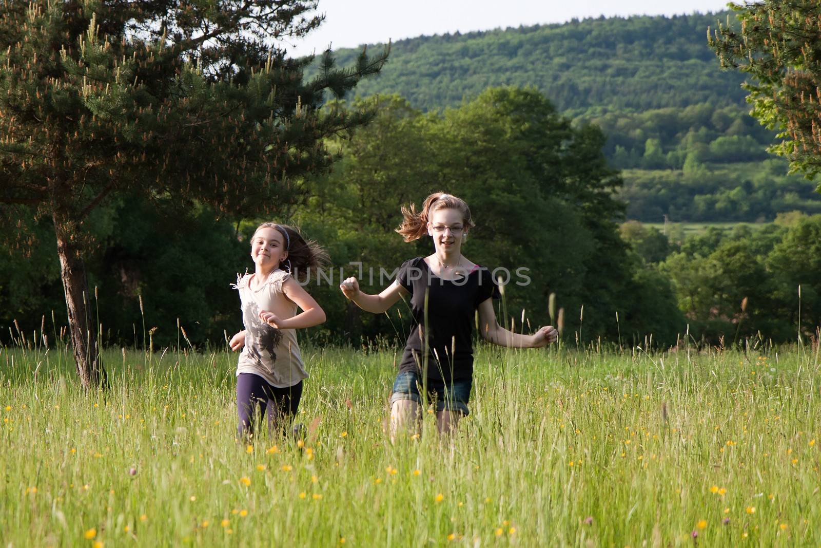 Two teens girls running in tall grass on a meadow