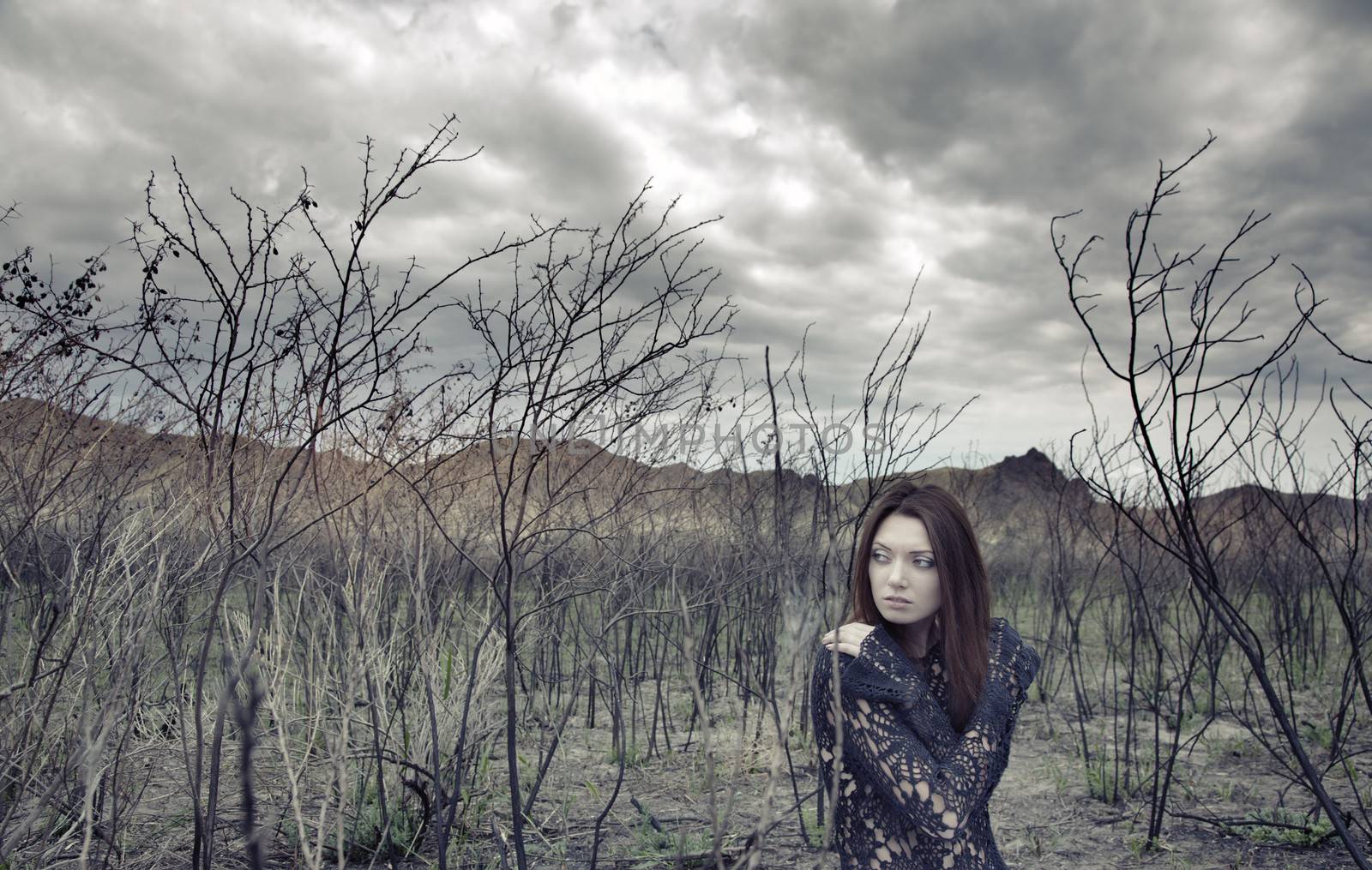 Sad alone woman in the dead bushes and thunderous sky on a background. Artistic colors added for movie effect
