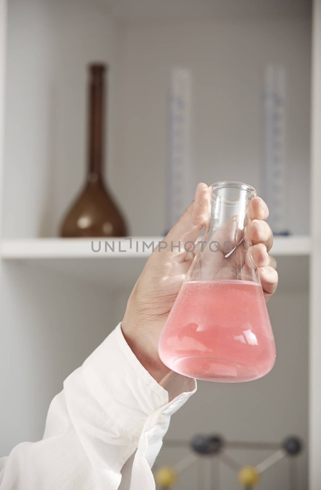 Hand of laboratory technician holding flask with red liquid