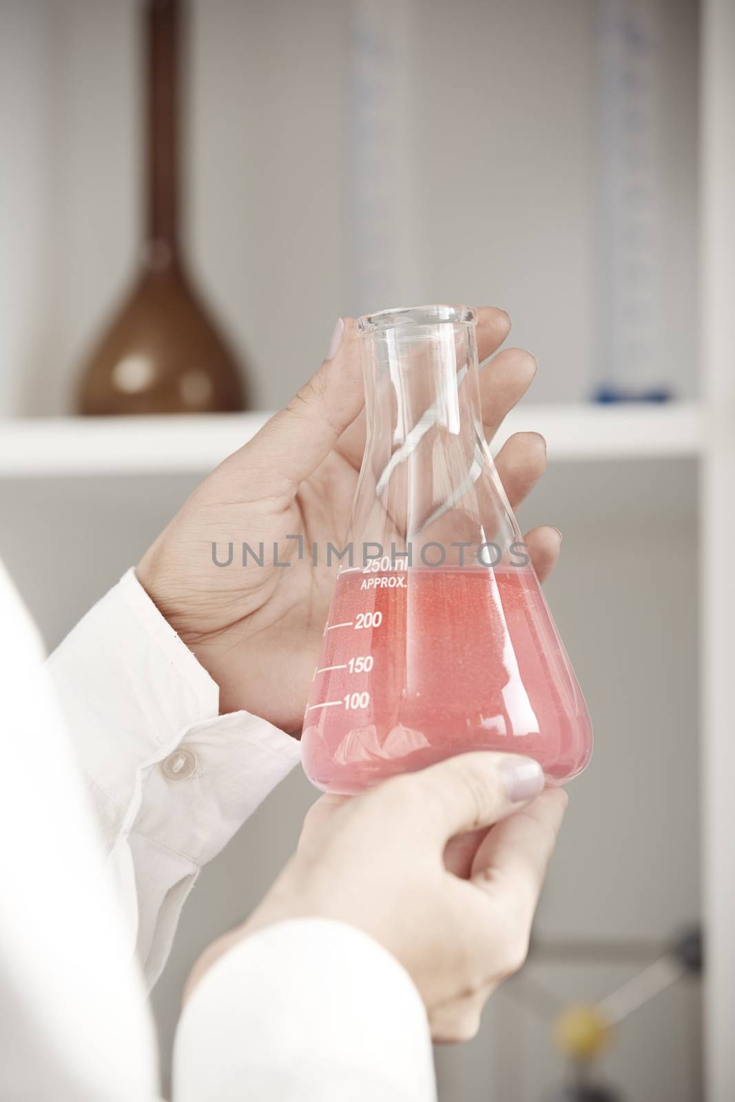 Hands of laboratory technician holding flask with red liquid