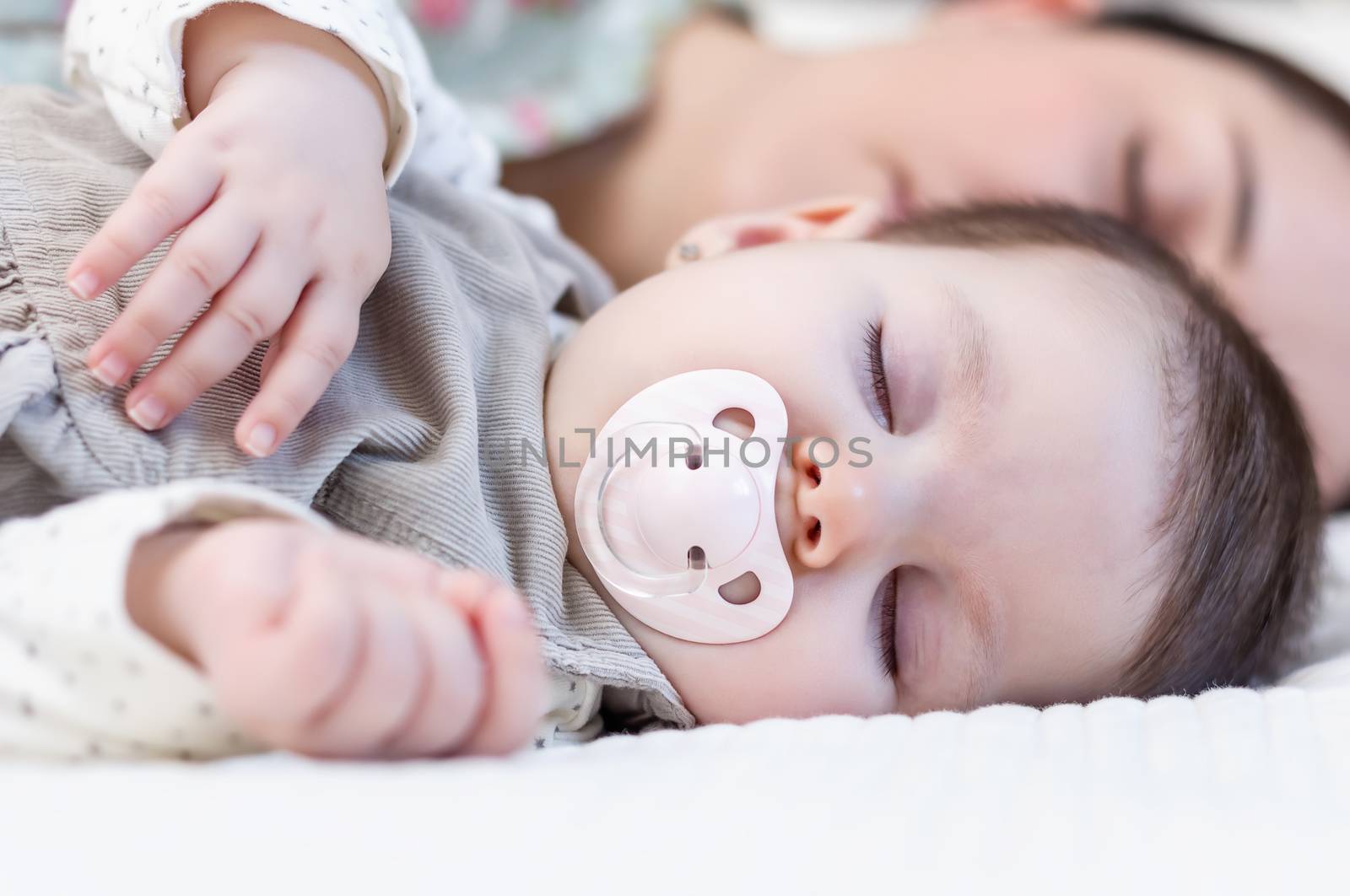 Young mother and her cute baby girl sleeping together in the bed