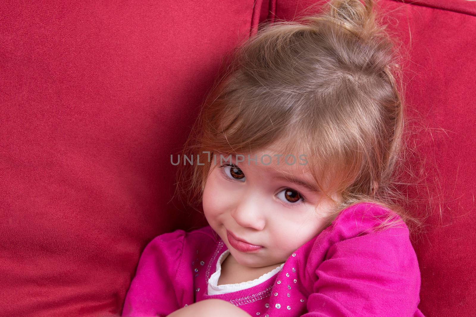 Shy little girl looking at the camera with big eyes as she snuggles down in a comfortable armchair