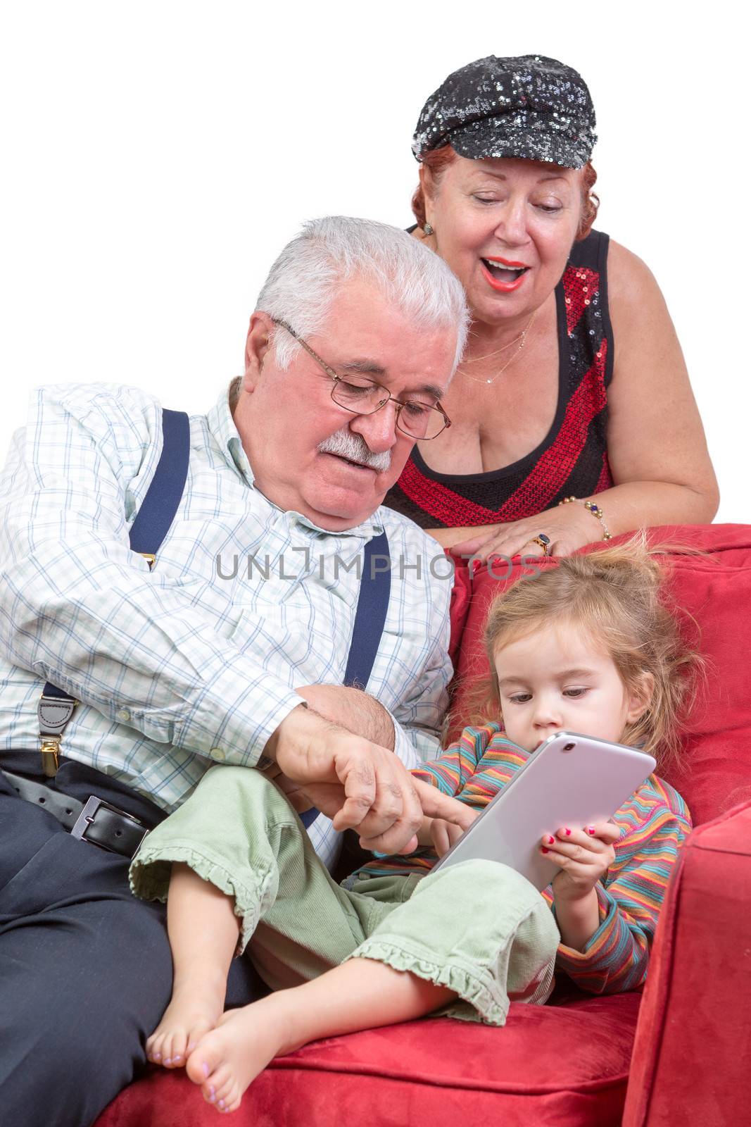 Grandparents babysitting their granddaughter sitting together ion a couch pointing out information on the tablet computer to her as they enjoy an e-book together