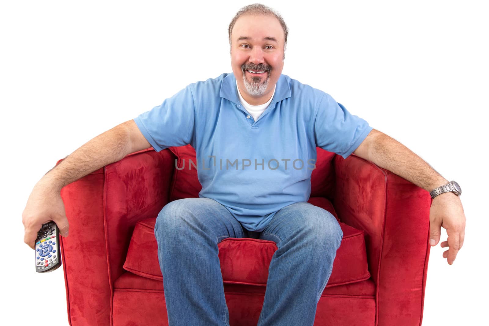 Funny cheerful middle-aged Caucasian man wearing casual clothes while sitting on a red comfortable armchair holding the remote control, on white background