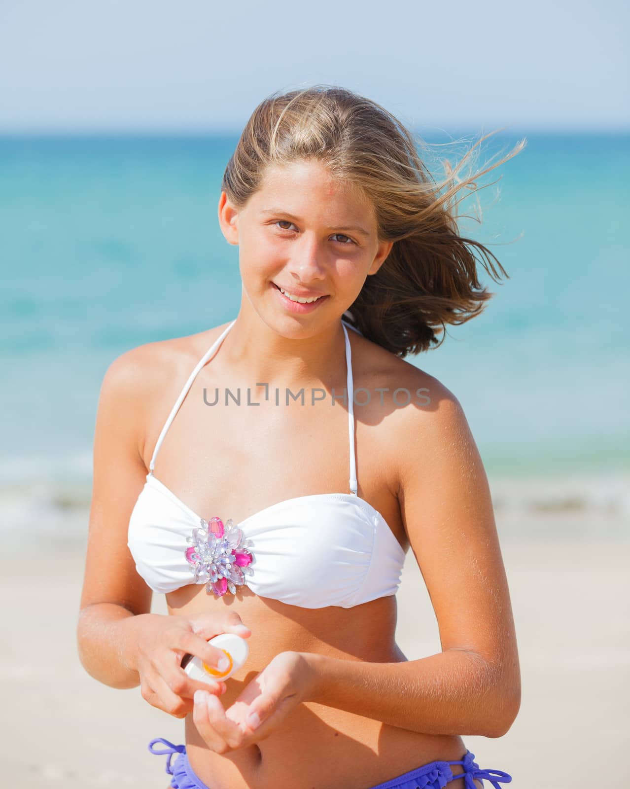 Beautiful young girl applying sunblock while sitting on a beach in summer.