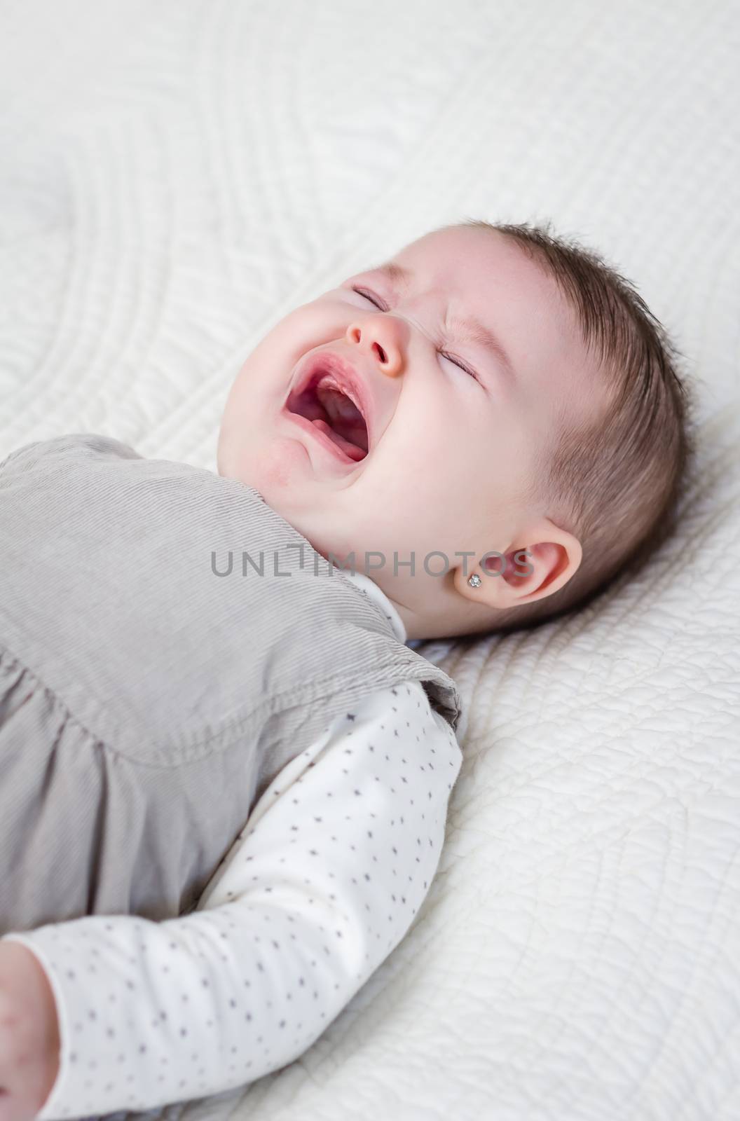 Cute baby girl crying over white bedcover