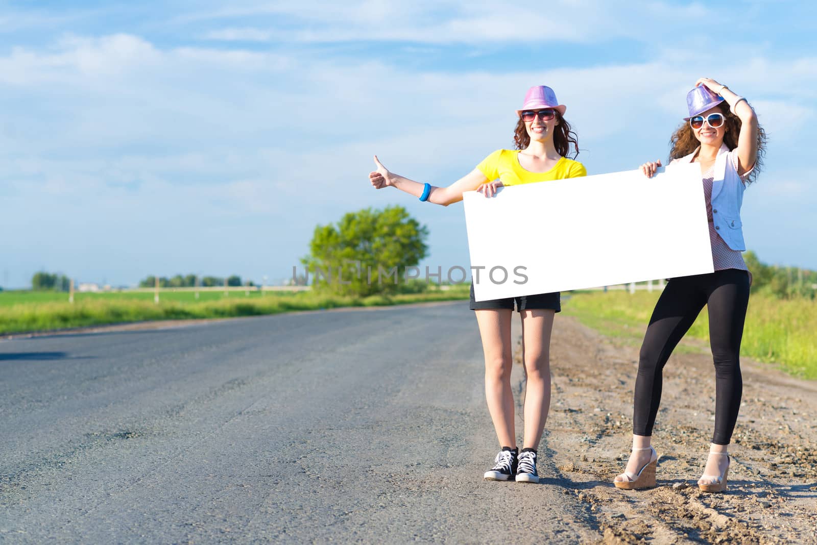 Two young women stand with a blank banner on the side of the road, place for text