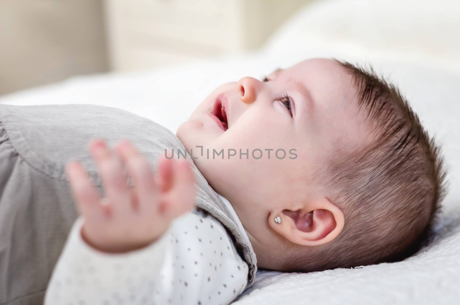 Cute baby girl crying over white bedcover