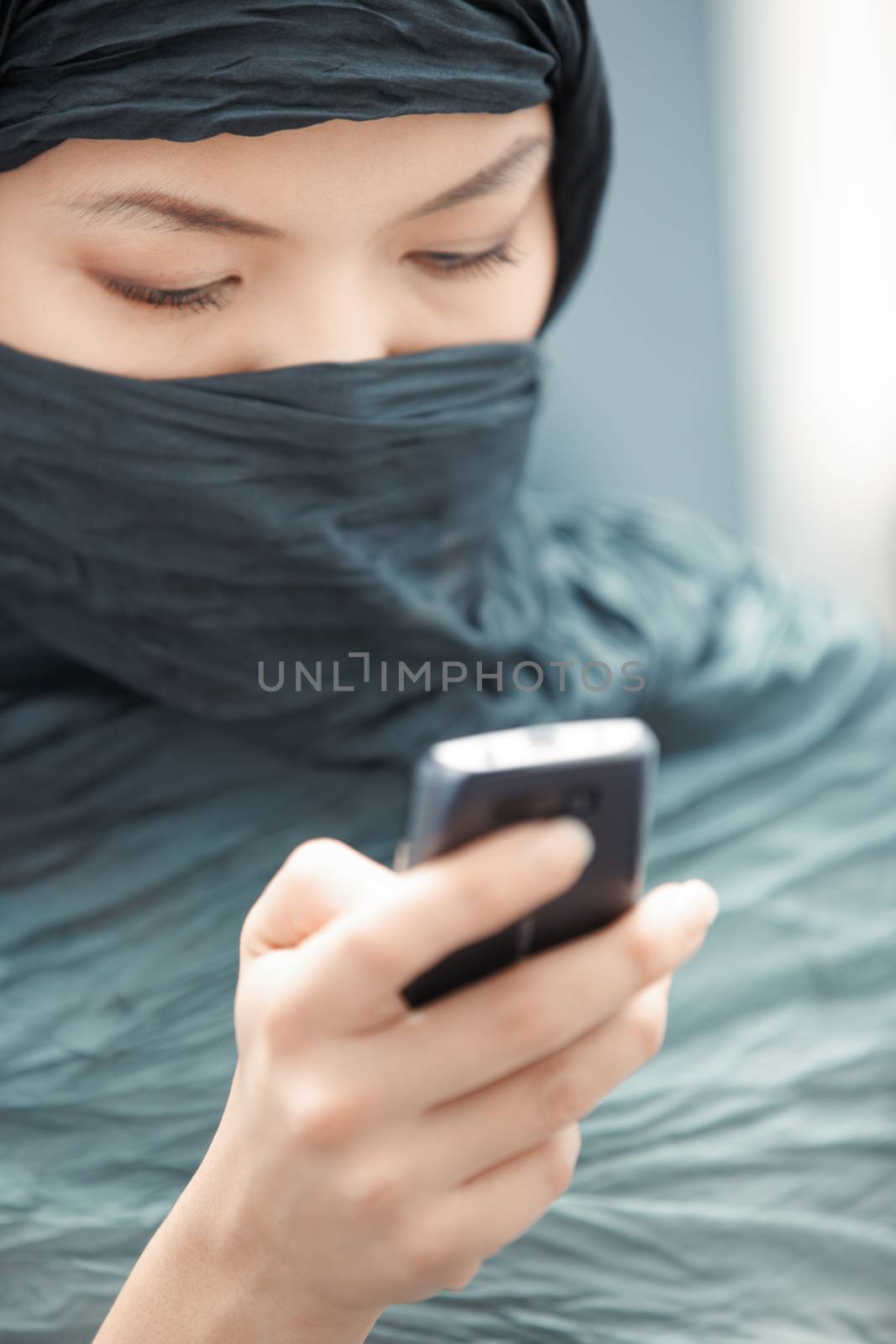Oriental lady in hijab sending SMS via cell phone