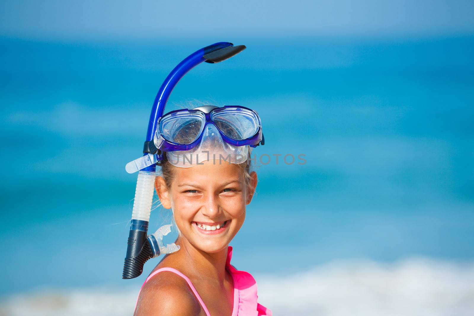 Portrait of happy girl on beach with blue face masks and snorkels, sea in background.