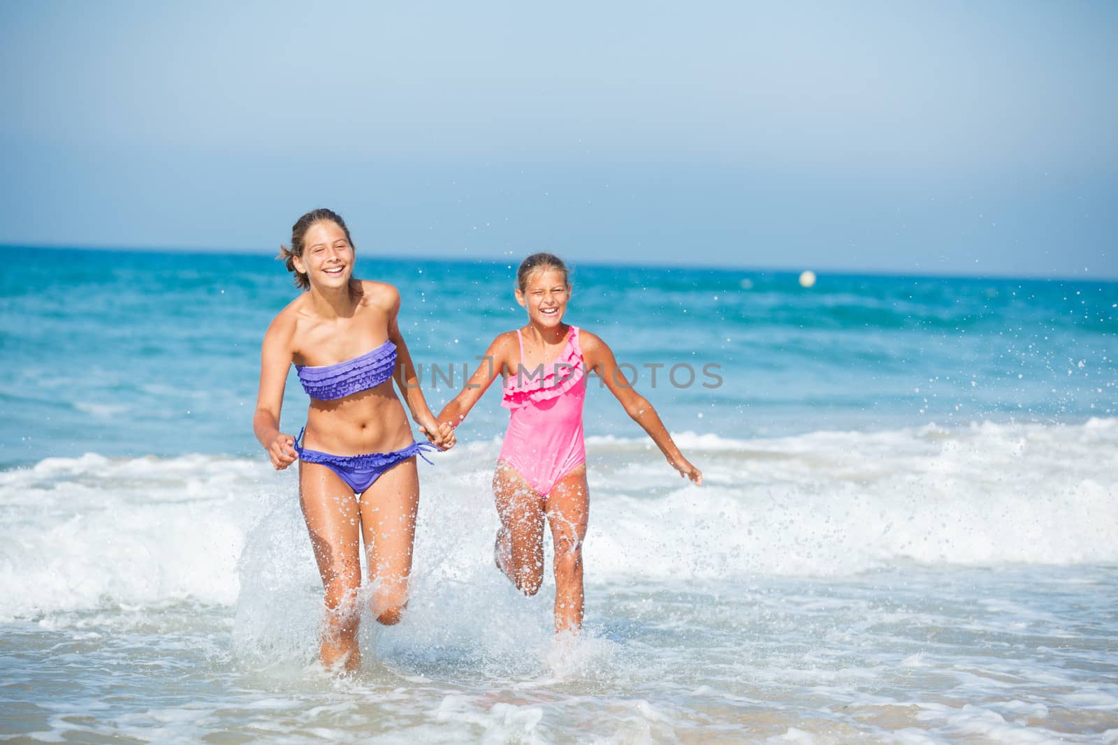 Cute girls friends running together in the beach shore on summer vacation