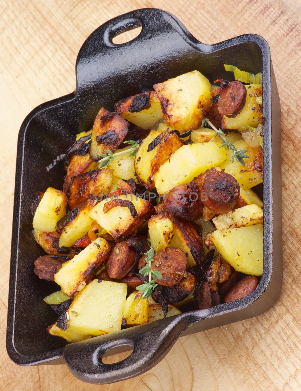 Tasty Homemade Roasted Sausages and Potato Stew in Frying Pan isolated on Wooden background