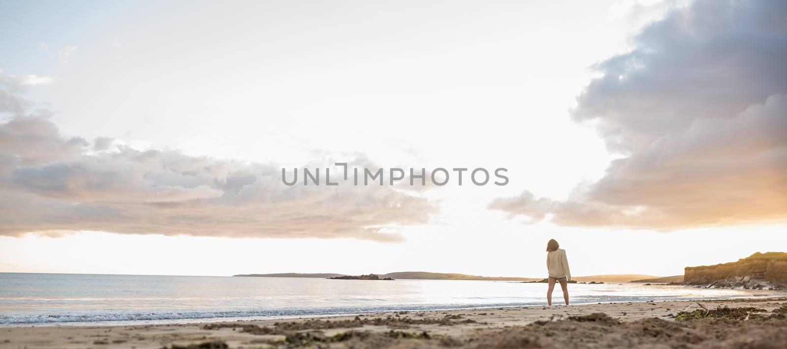 Full length of a young woman in sweater walking on the beach