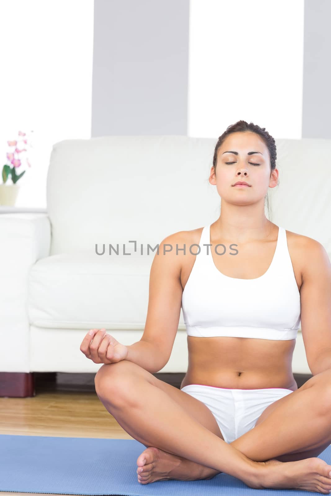 Brunette woman in sportswear sitting on an exercise mat meditating in her living room