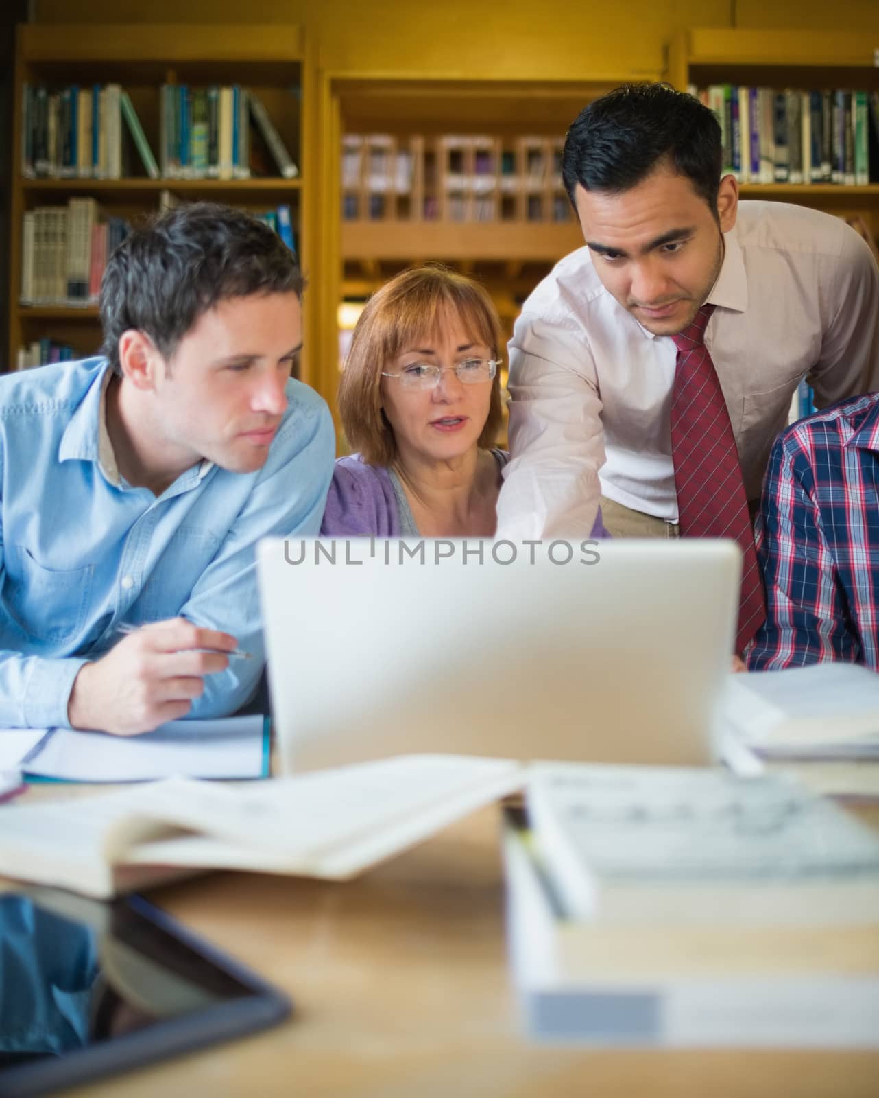 Mature students with teacher and laptop in library by Wavebreakmedia