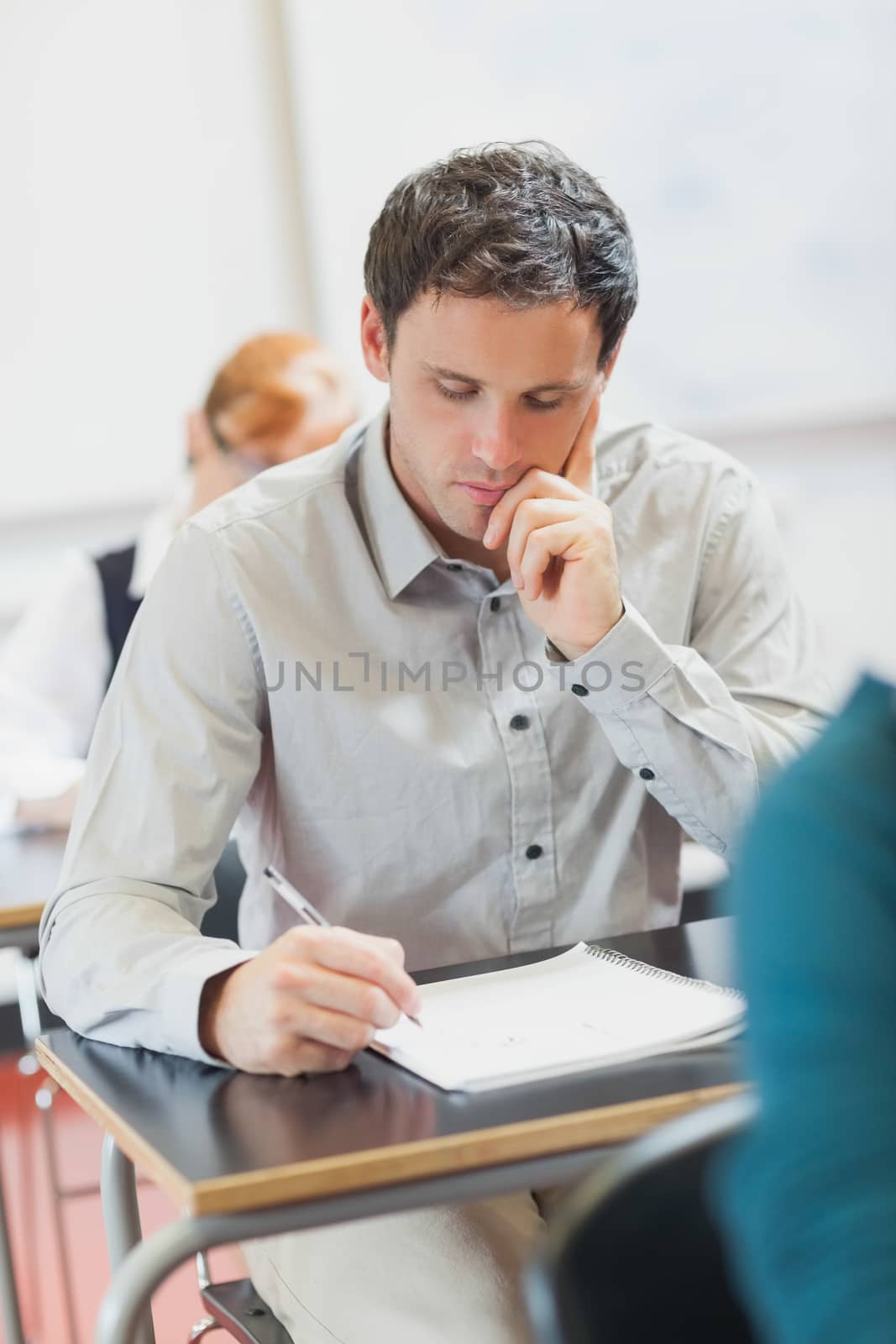 Focused handsome mature student sitting in classroom with classmates while learning