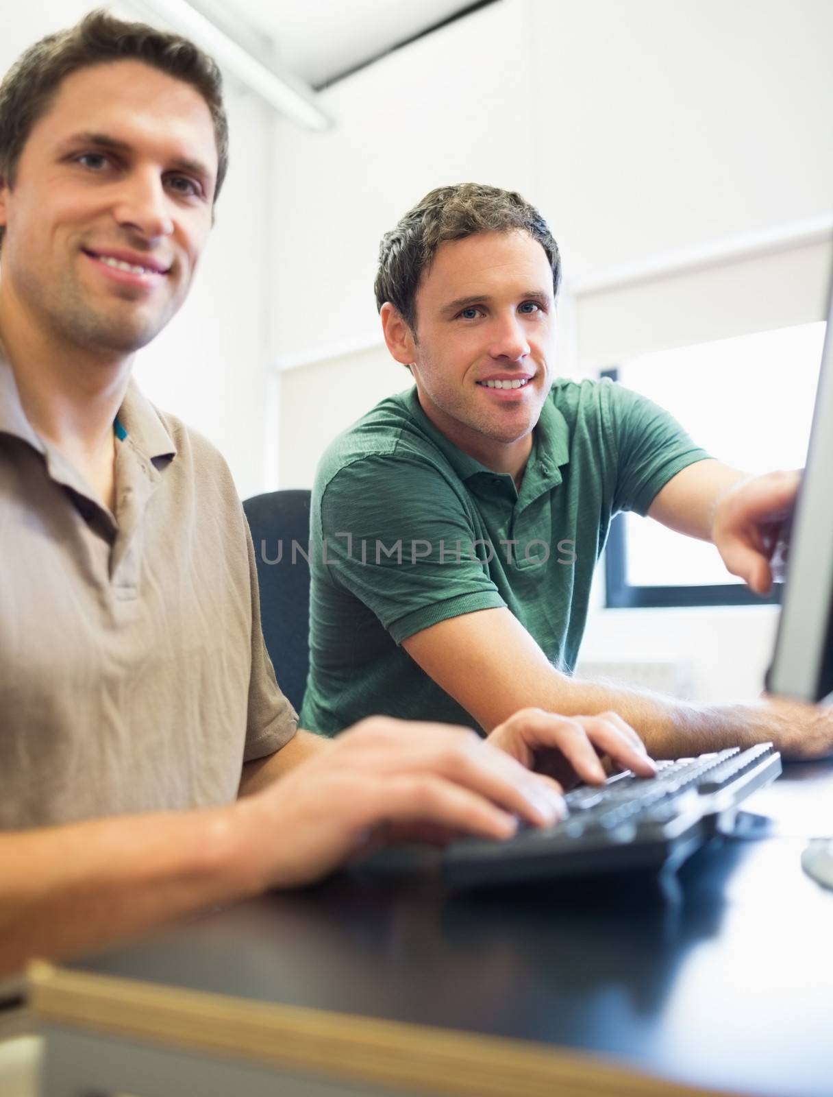 Portrait of smiling teacher showing something on screen to mature student in the computer room