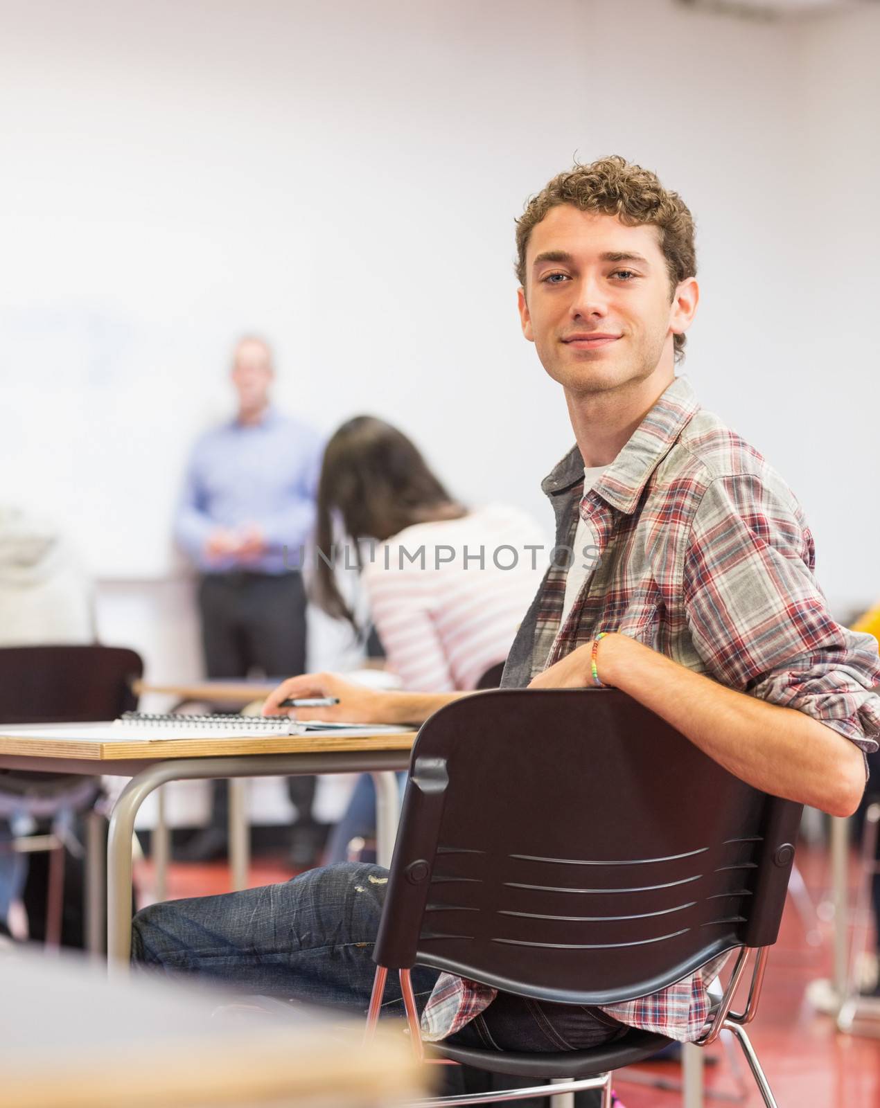 Portrait of a smiling young male student with blurred teachers and others in the classroom