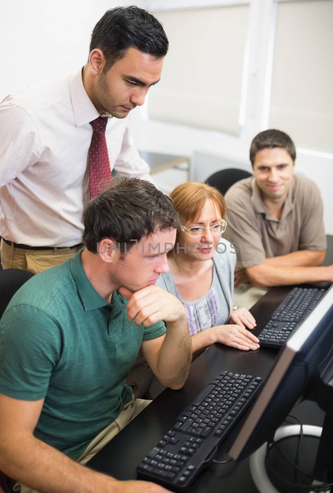 Concentrated teacher looking at mature students use computer in the computer room