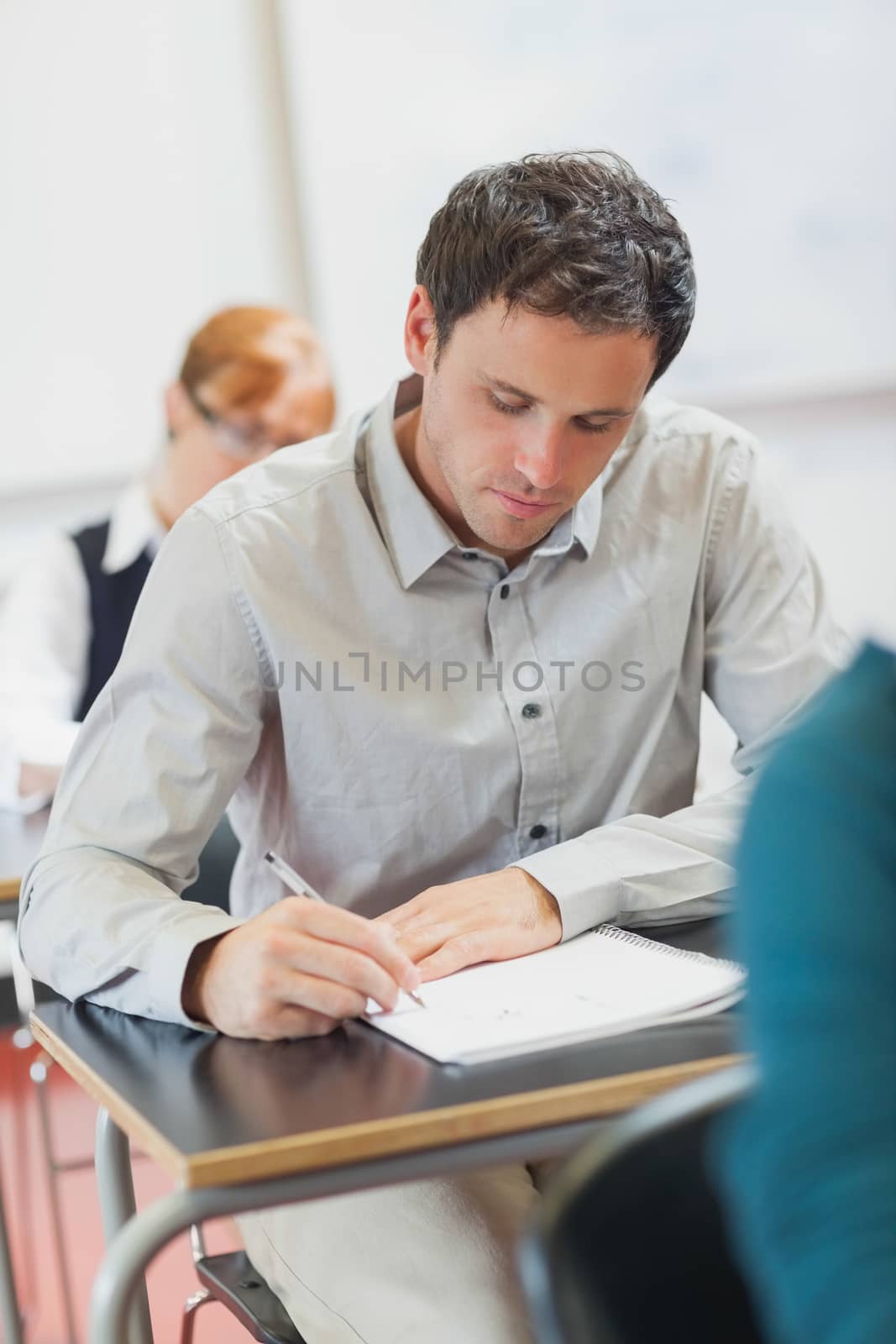 Concentrated male mature student sitting in classroom with classmates by Wavebreakmedia