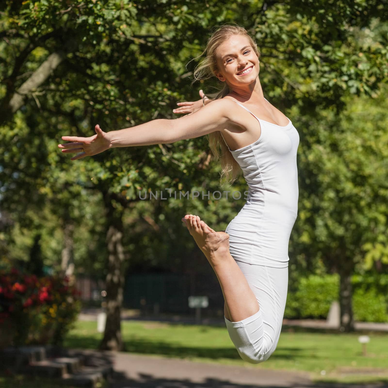 Side view of young fit woman jumping spreading her arms in a park