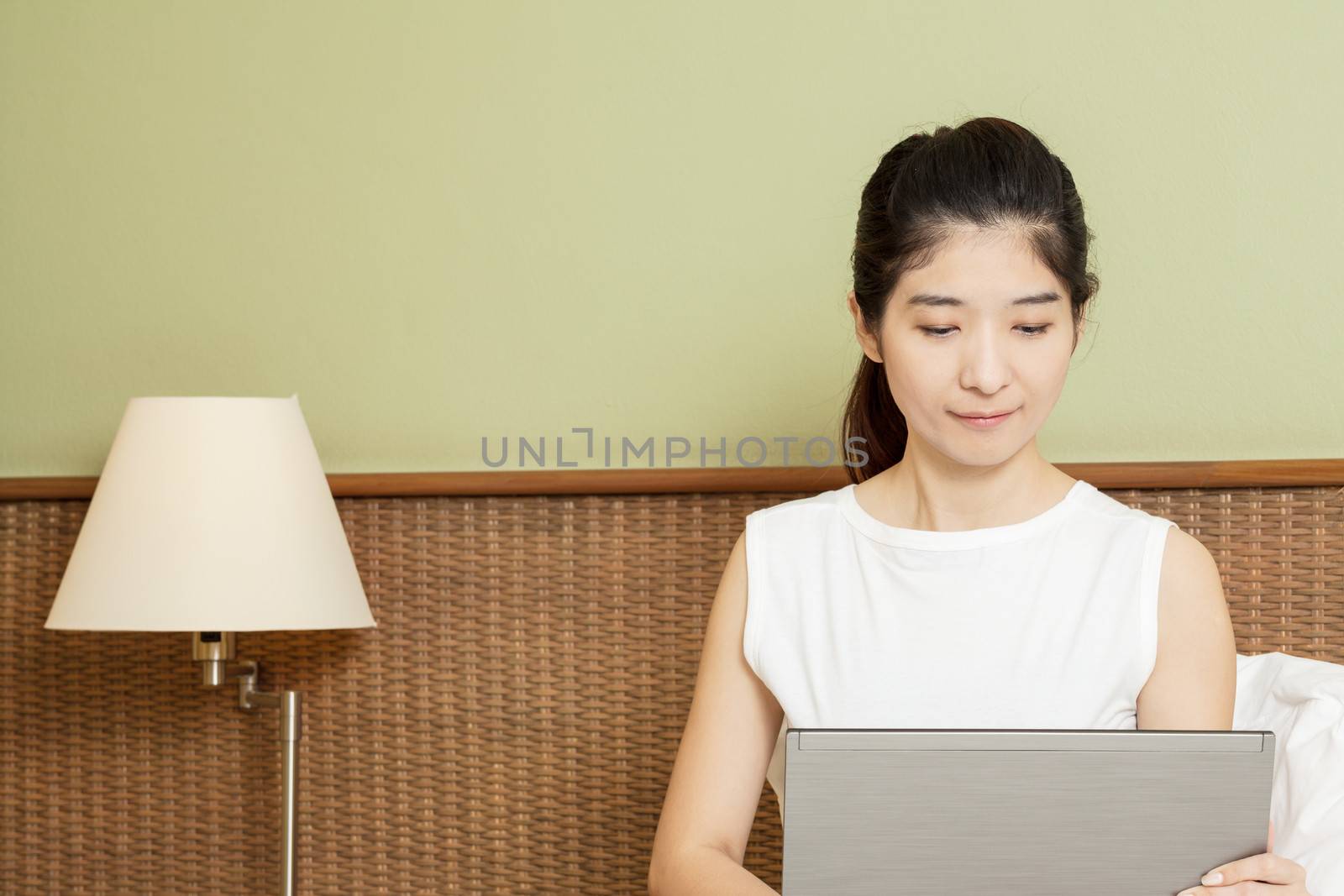 happy young asian woman working with laptop in bedroom by FrameAngel