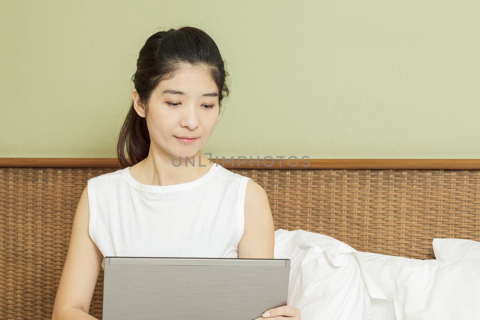 happy young asian woman working with laptop in bedroom by FrameAngel