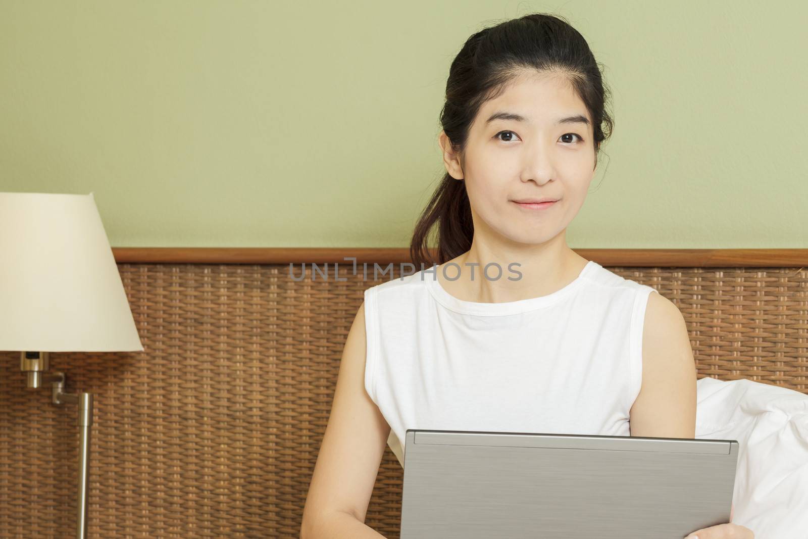 happy young asian woman working with laptop in bedroom by FrameAngel