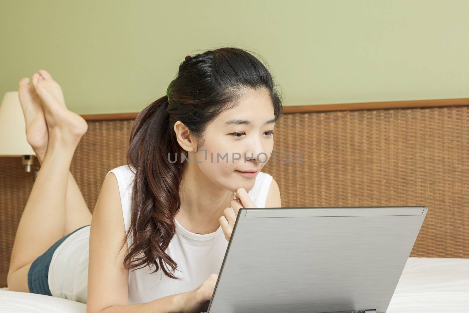 happy young asian woman working with laptop in bedroom by FrameAngel