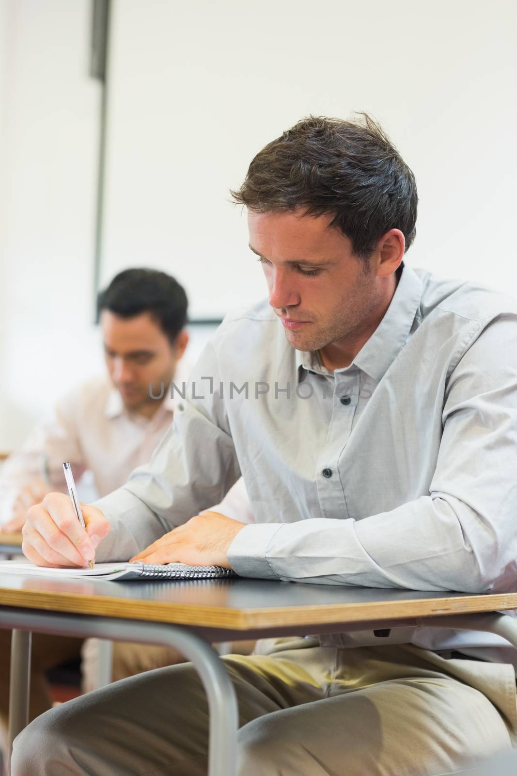 Mature students taking notes in classroom by Wavebreakmedia