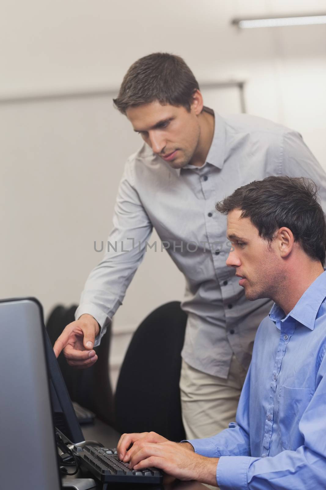 Handsome teacher talking to a student in computer class