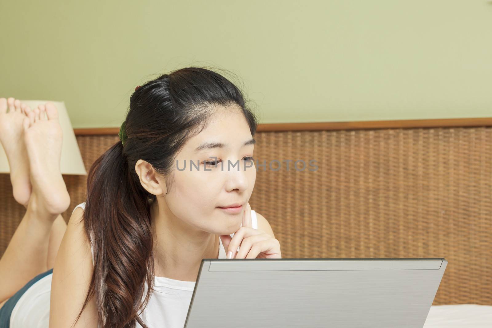 happy young asian woman working with laptop in bedroom by FrameAngel