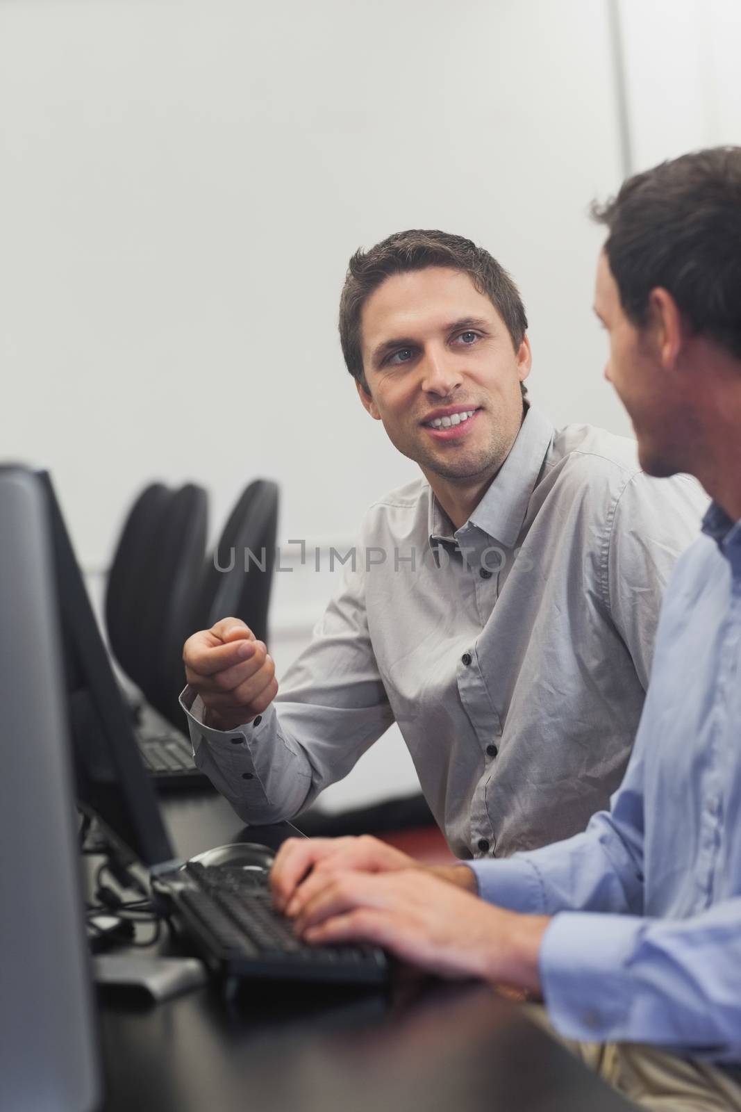 Two friendly men talking sitting in front of a computer in computer class