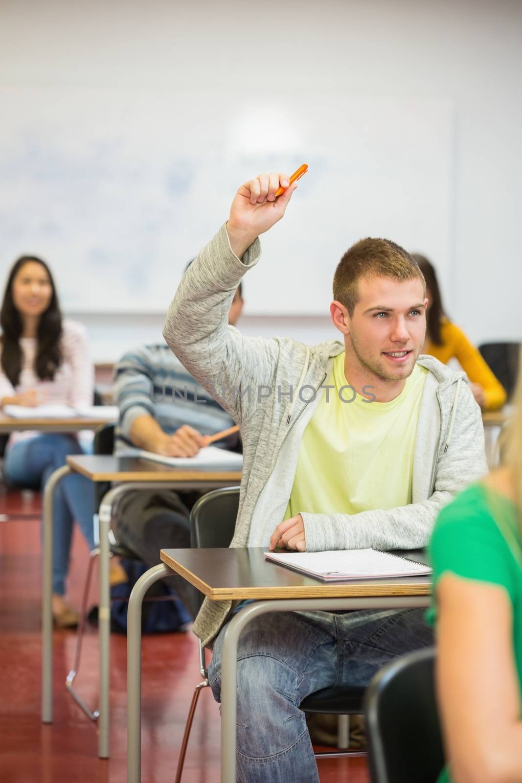 Young male student raising hand by others in the college classroom