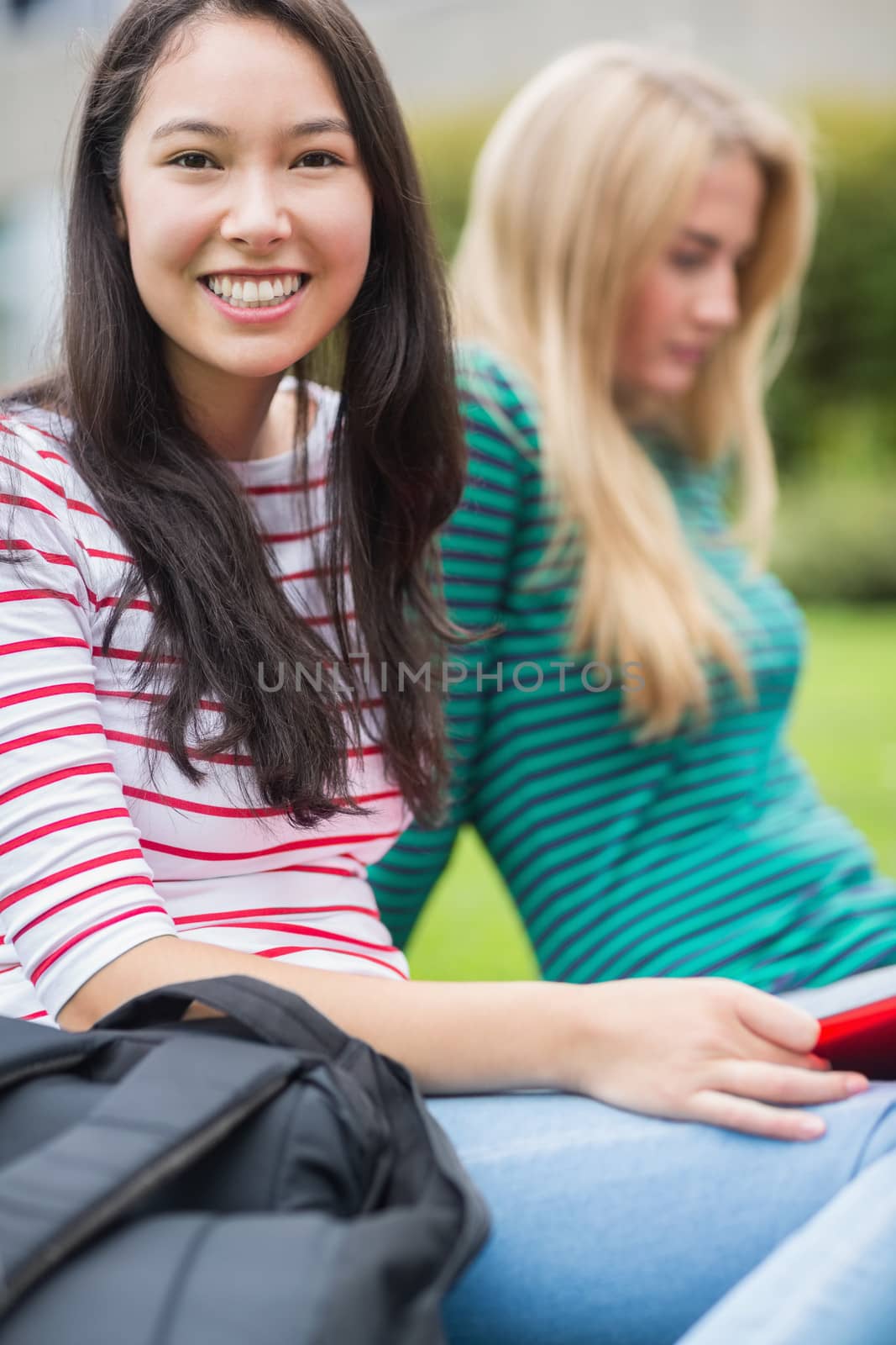 Portrait of a smiling young college student with blurred friend sitting in the park