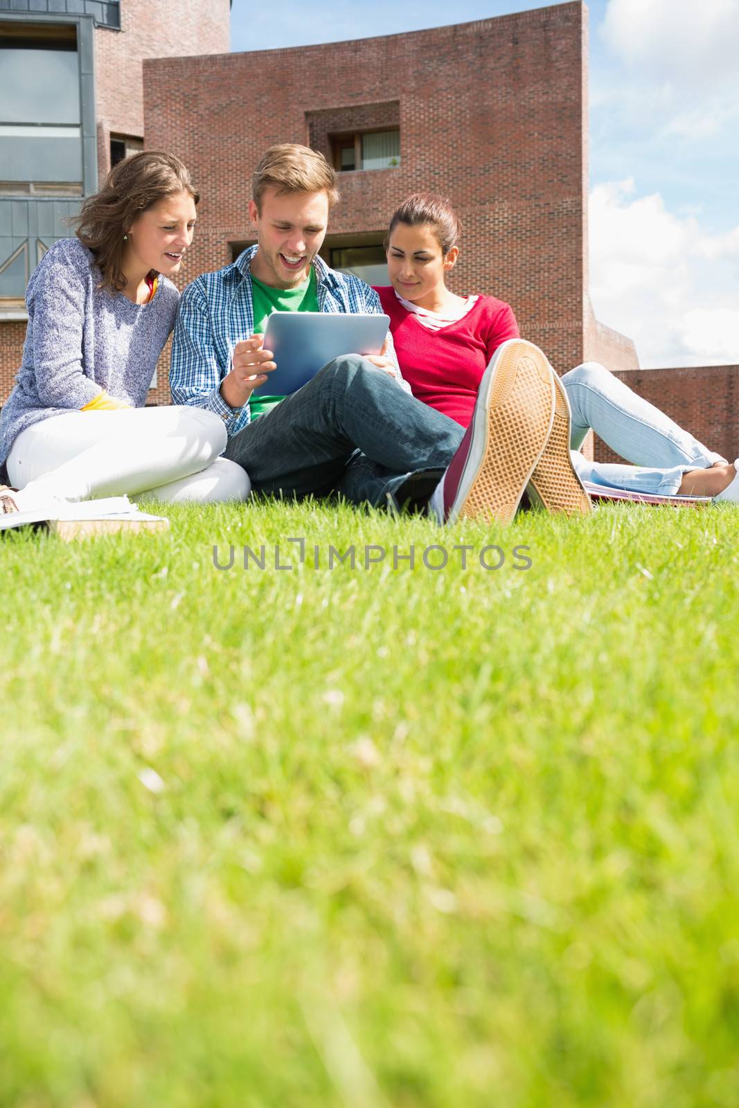 Students using tablet PC in the lawn against college building by Wavebreakmedia