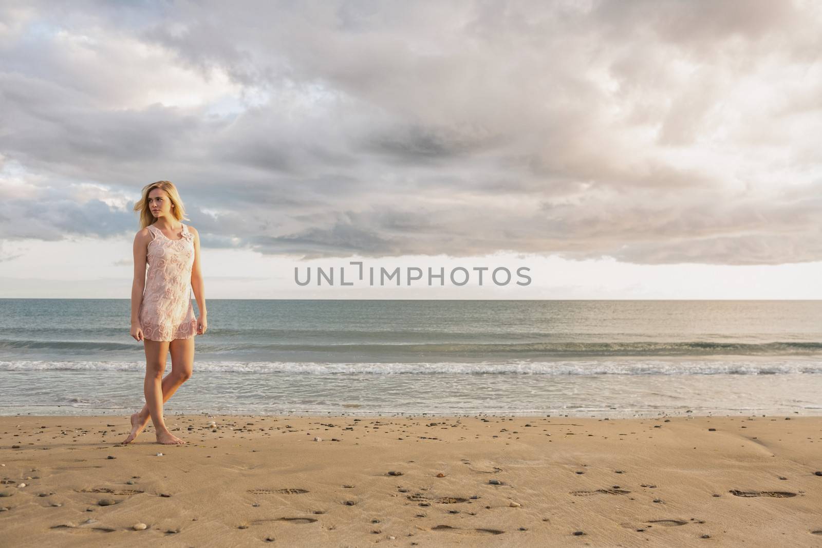 Full length of a pretty young woman in summer dress walking on the beach
